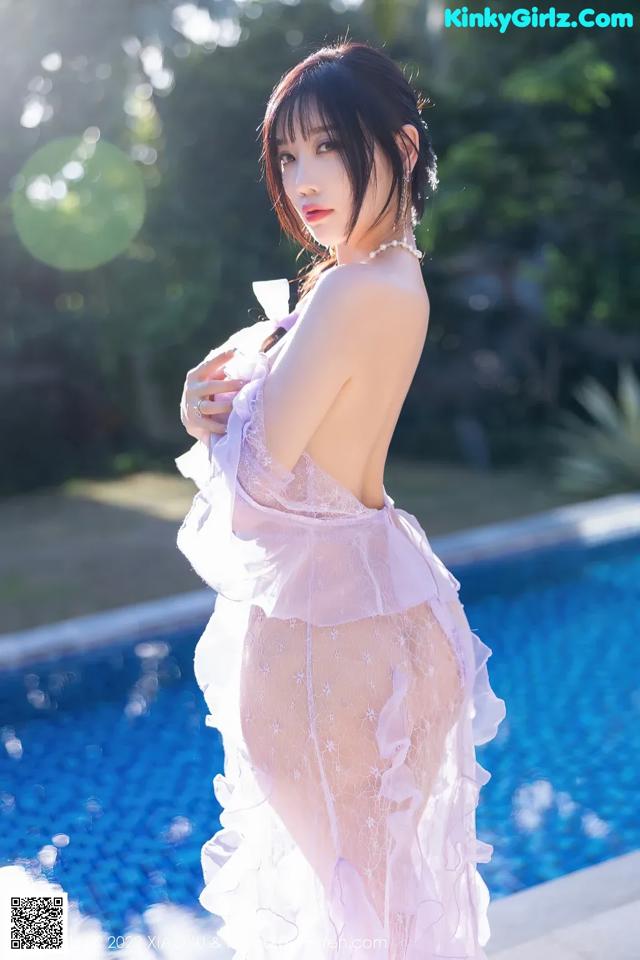 A woman in a white dress standing next to a swimming pool.