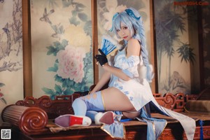 A woman in a blue and white outfit sitting on a wooden floor.