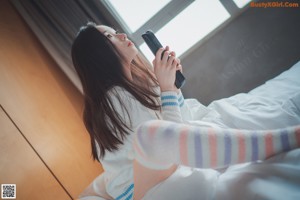 A woman sitting on a bed in a white sweater and striped stockings.