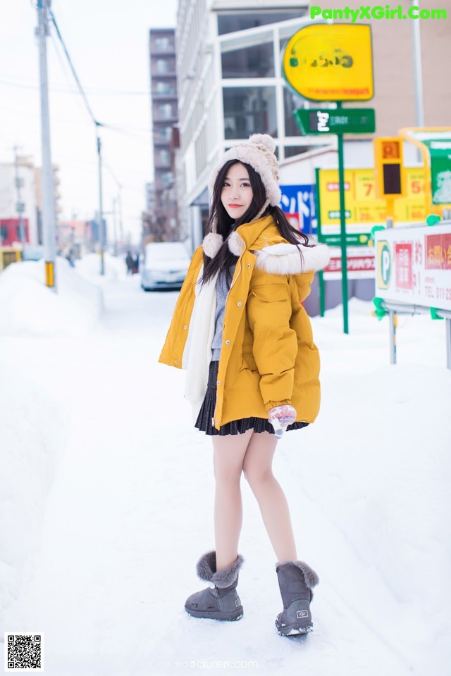 A woman in a yellow coat is standing in the snow.