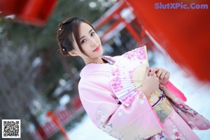 A woman in a pink fur coat posing on a wooden deck.