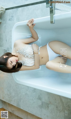 A woman in a white lingerie sitting in a bathtub.