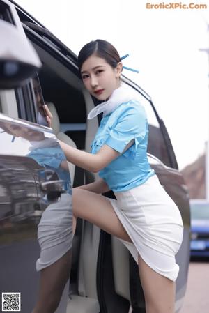 A woman in a blue shirt and white skirt standing next to a car.