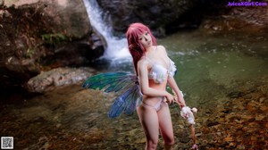 A woman with pink hair and a fairy wings sitting in the water.
