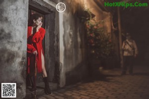 A woman in a red robe standing in an alleyway.