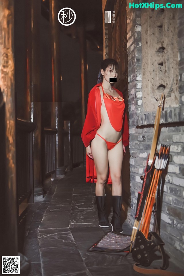 A woman in a red robe standing next to a brick wall.