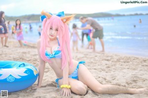 A woman with pink hair wearing a blue bikini on the beach.