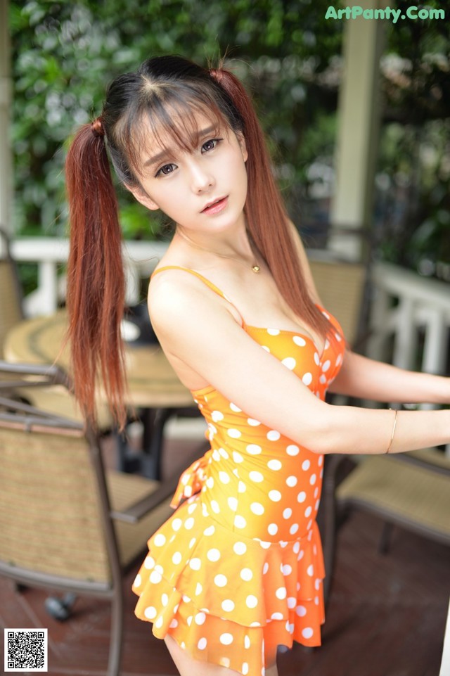 A woman in an orange polka dot dress posing for a picture.
