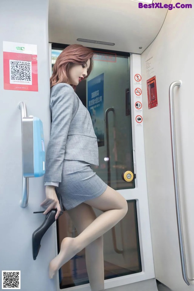 A woman in a gray suit is standing on a train.