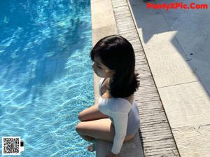 A woman in a bathing suit standing on a beach next to a pool.