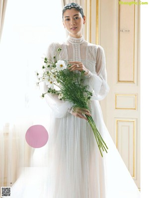 A woman in a white wedding dress holding a bouquet of flowers.